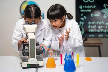 Two focused girls examine a sample using a microscope. The look of surprise on one face captures the thrill of discovery in the microscopic world during their experiment.