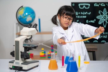 A student in a lab coat and glasses stretches orange slime, clearly enjoying the hands-on chemistry. Colorful beakers and a microscope highlight a fun, engaging learning environment.