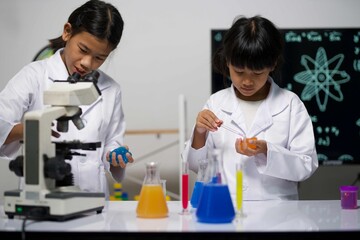 Two girls collaborate in the lab; one pipettes liquid, the other holds blue slime. Their teamwork reflects shared excitement in exploring science and chemical reactions.