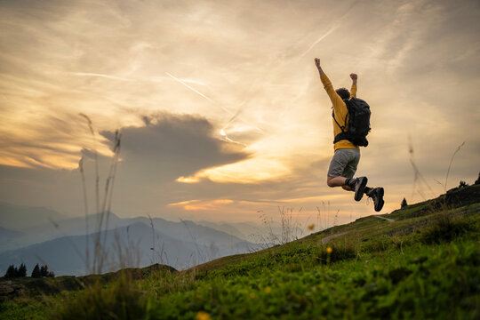 Carefree man jumping with arms raised on mountain at sunrise