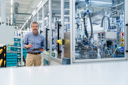 Engineer with clipboard in automated factory next to industrial robot