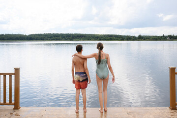 Friends in swimsuits standing on lakeside dock in summer rear view