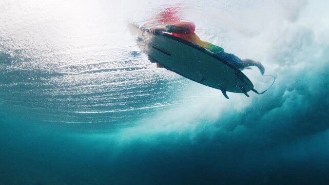 Surfer under the wave. Underwater view of the teen boy surfer diving under the wave with surf board