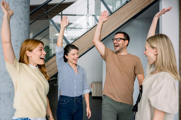 Smiling team celebrating success with raised hands in modern office