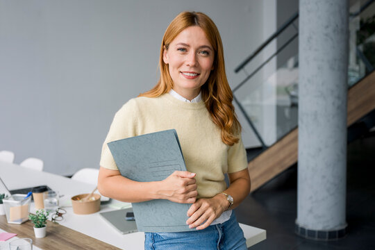 Confident businesswoman smiling with folder at modern office