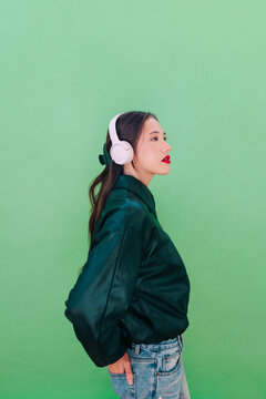 Side view of woman with pink headphones and dark jacket against green