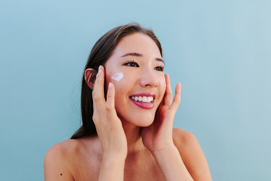 Smiling woman applying skincare cream on face in studio portrait
