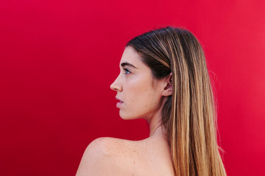 Woman with straight hair in side profile against red background