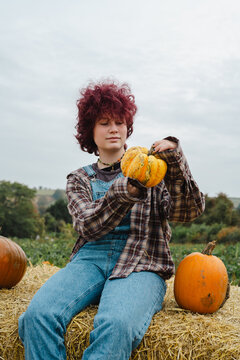 Teenager with curly hair holding pumpkin at autumn pumpkin patch outdoors