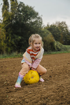 Child sitting on giant yellow pumpkin in autumn pumpkin patch outdoors