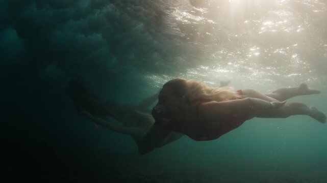 Three young sensual women in red swim suits dive under the breaking ocean wave