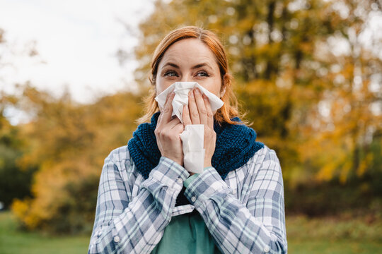 Woman blowing nose with tissue outdoors during autumn allergy season