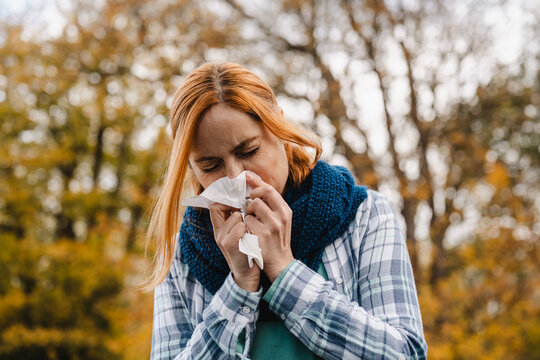 Woman blowing nose outdoors in autumn with cold symptoms