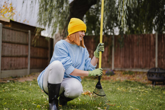 Person raking leaves in autumn garden with gloves and yellow hat
