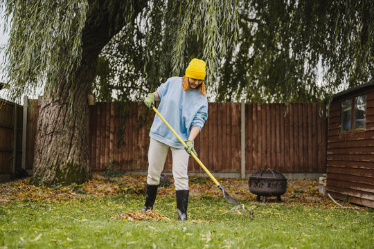 Person raking garden waste in backyard during autumn for recycling