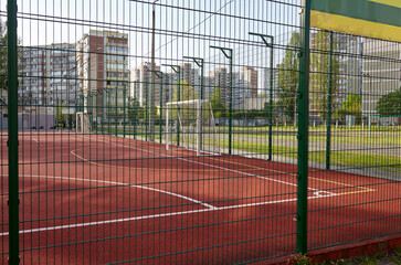 Сoated field for playing football behind the green fence mesh at school territory. Close-up of soccer field with red floor