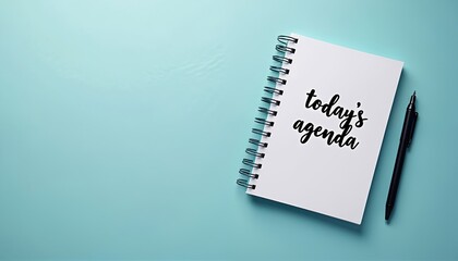Spiral bound notebook with text todays agenda, black pen on teal surface. Flat lay composition suggests planning, organization for current day. Empty space allows for customization. Suitable for