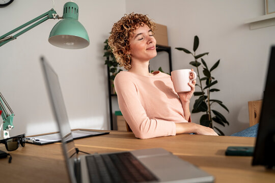 Relaxed woman enjoying coffee break at cozy home office workspace
