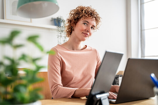 Focused woman at modern workspace with multiscreen laptop setup