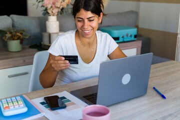 Woman shopping online with credit card at home office desk smiling