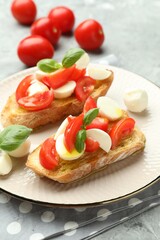 Tasty bruschettas with mozzarella cheese, tomatoes and basil on grey textured table, closeup