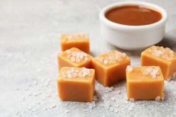Tasty candies with salt and caramel sauce on grey textured table, closeup. Space for text