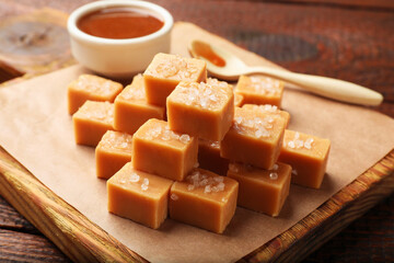 Tasty candies with salt, caramel sauce and spoon on wooden table, closeup