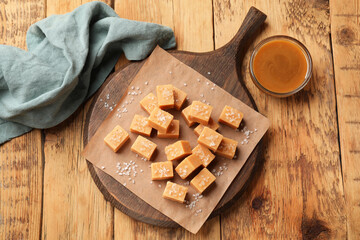 Tasty candies with salt and caramel sauce on wooden table, flat lay