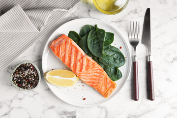 Piece of tasty grilled salmon, lemon slice and spinach served on white marble table, flat lay