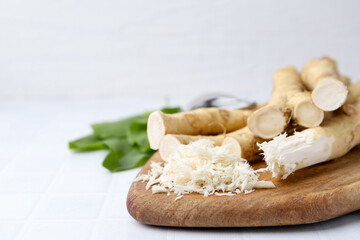 Grated horseradish and fresh roots on white tiled table, closeup. Space for text