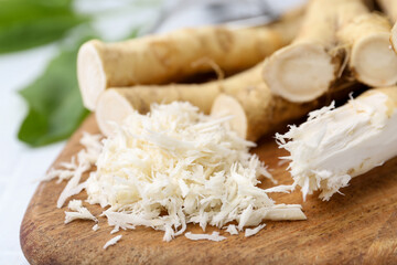 Grated horseradish, leaves and fresh roots on white table, closeup