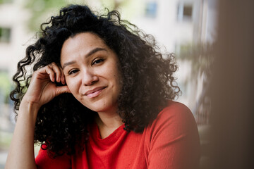 Pensive curly haired woman in red shirt outdoors on a sunny urban day
