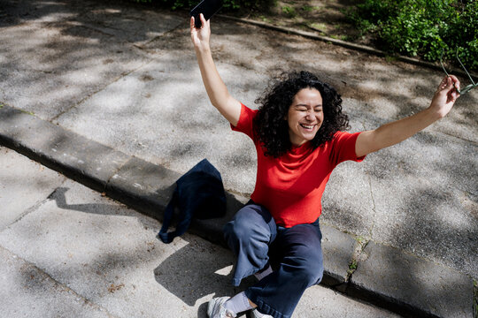 Happy woman sitting outdoors on sunny urban day celebrating