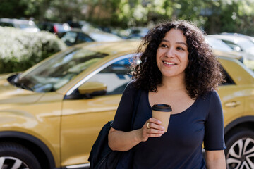Smiling woman enjoying coffee to go on sunny summer urban street