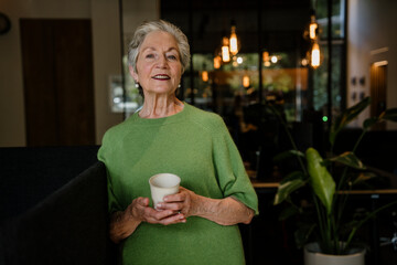 Happy business owner in green sweater holding coffee cup in modern office