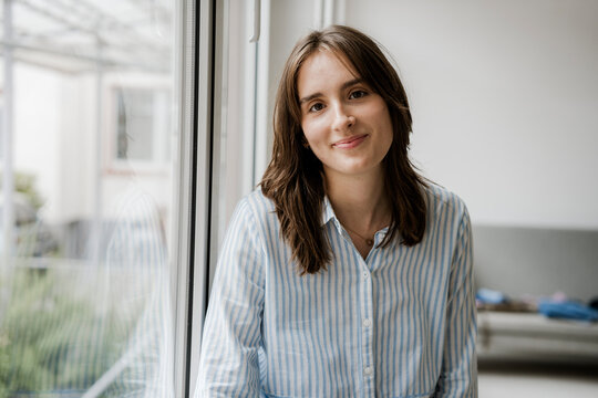 Portrait of a relaxed smiling woman in striped shirt by window indoors