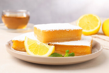 Tasty lemon bars with mint, fresh fruits and tea on beige table, closeup