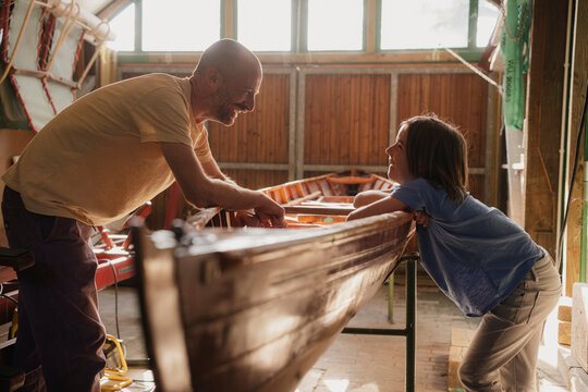 Father and son enjoy crafting a wooden boat together in a sunny workshop