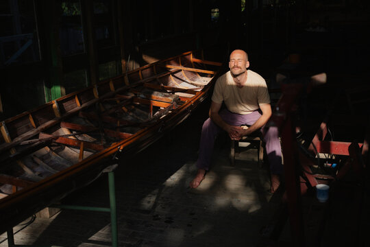 Man taking a break in sunlight by wooden boat in workshop
