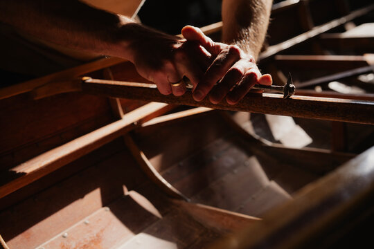 Hands working on wooden boat craft in sunlight showing detail and tranquility