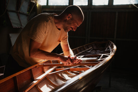 Smiling man working on wooden boat in sunny indoor workshop