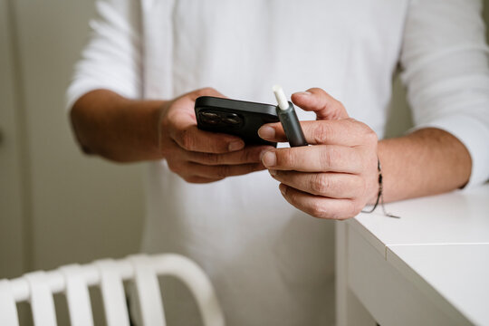 Man holding vape and smartphone indoors at home during coffee break