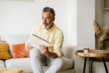 Man sitting on sofa at home holding a calendar and looking at camera