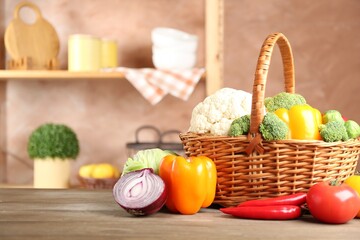 Different fresh raw vegetables in wicker basket on wooden table indoors, closeup. Space for text