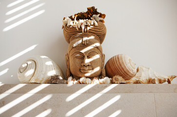 Buddha head decorated with shells in interior under sunlight
