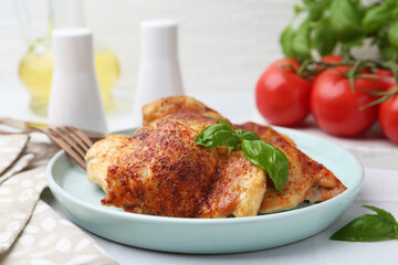 Tasty roasted chicken thighs with basil served on white tiled table, closeup