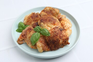 Tasty roasted chicken thighs with basil on white tiled table, closeup