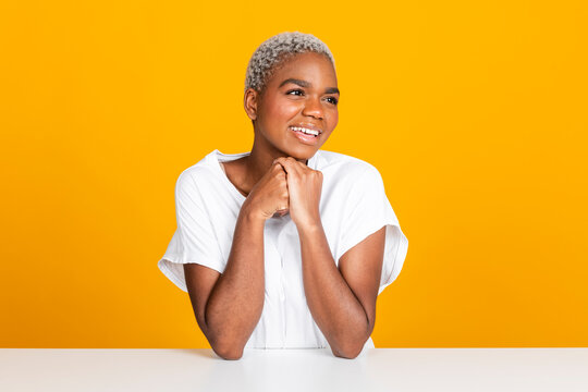 Happy young woman sitting with hands clasped at table against yellow background