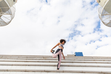 Young woman standing on steps and stretching foot under cloudy sky