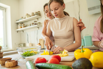 Woman helping girl prepare salad together in cozy home kitchen